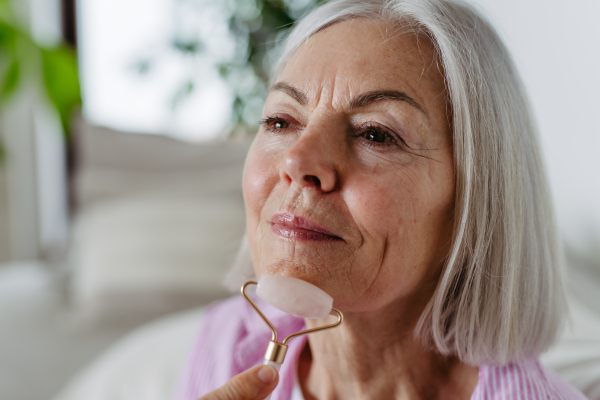 Skincare routine for mature woman. Older woman using facial roller for blood circulation, after serum.