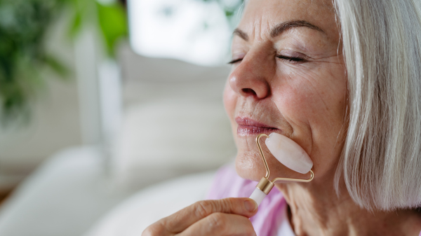 Skincare routine for mature woman. Older woman using facial roller for blood circulation, after serum.