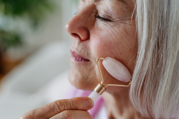 Skincare routine for mature woman. Older woman using facial roller for blood circulation, after serum.