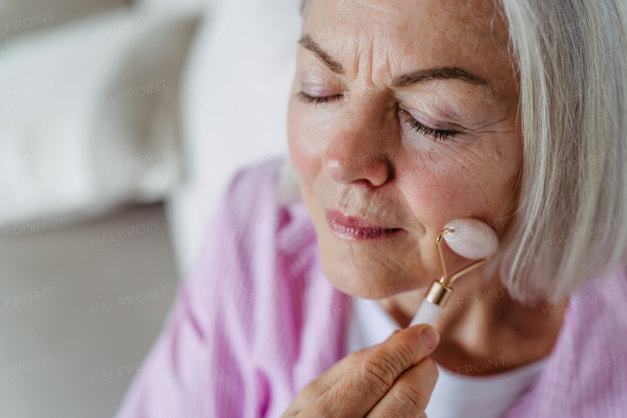 Skincare routine for mature woman. Older woman using facial roller for blood circulation, after serum.