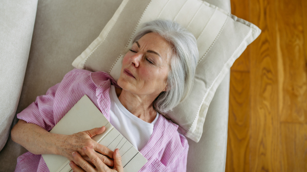 Top view of a beautiful mature woman asleep with book. Weekend activity for older woman, relaxing at home.