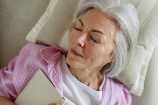 Top view of a beautiful mature woman asleep with book. Weekend activity for older woman, relaxing at home.