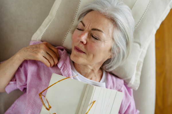 Top view of a beautiful mature woman asleep with book. Weekend activity for older woman, relaxing at home.