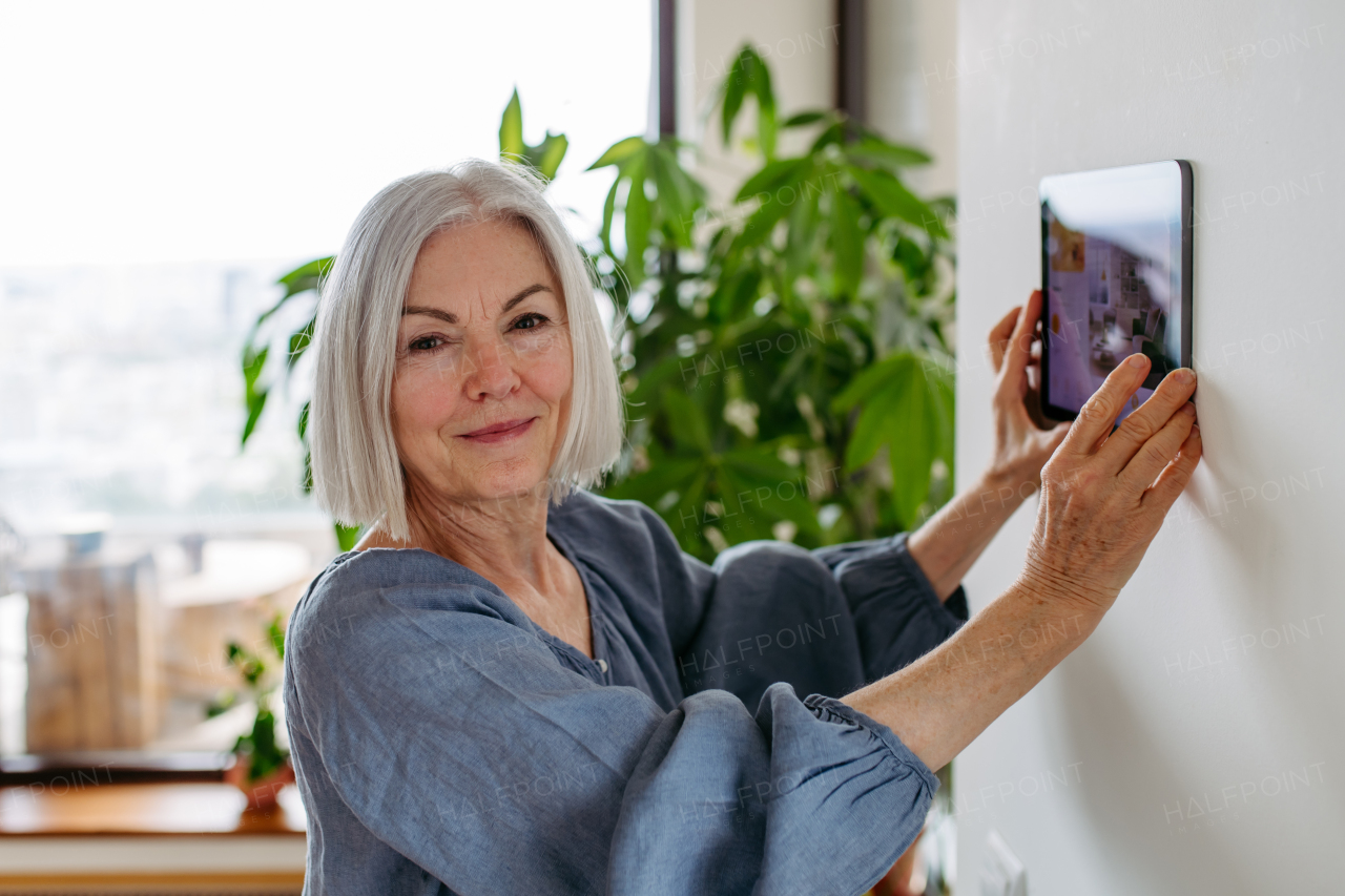 Mature woman adjusting household functions, lighting, security cameras, door locks, smart thermostat or heating settings. Concept of sustainable and smart technology at home.