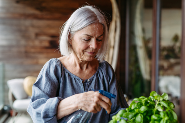 Portrait of beautiful mature woman taking care of plants, herbs on balcony. Spending free weekend at home, stay in.