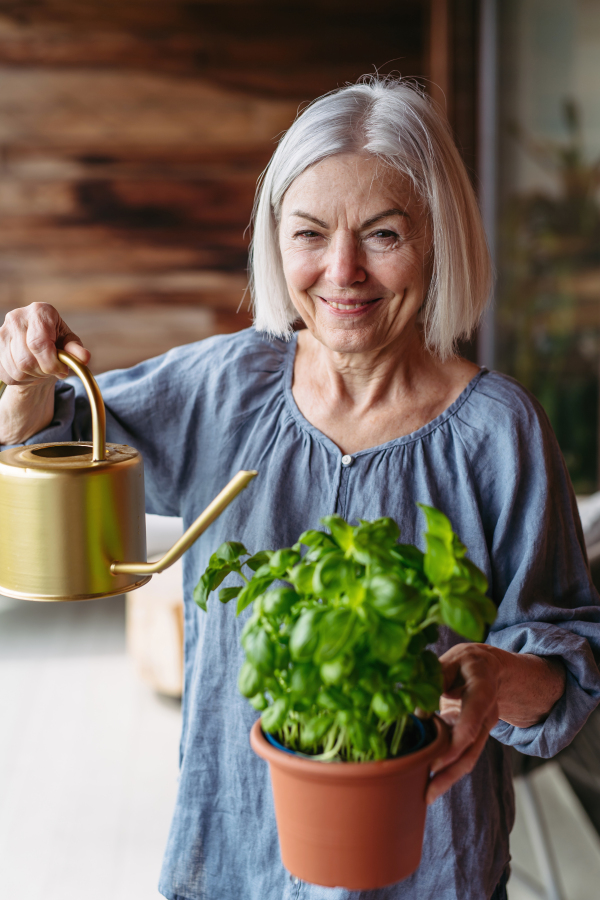 Portrait of beautiful mature woman taking care of plants, herbs on balcony. Spending free weekend at home, stay in.