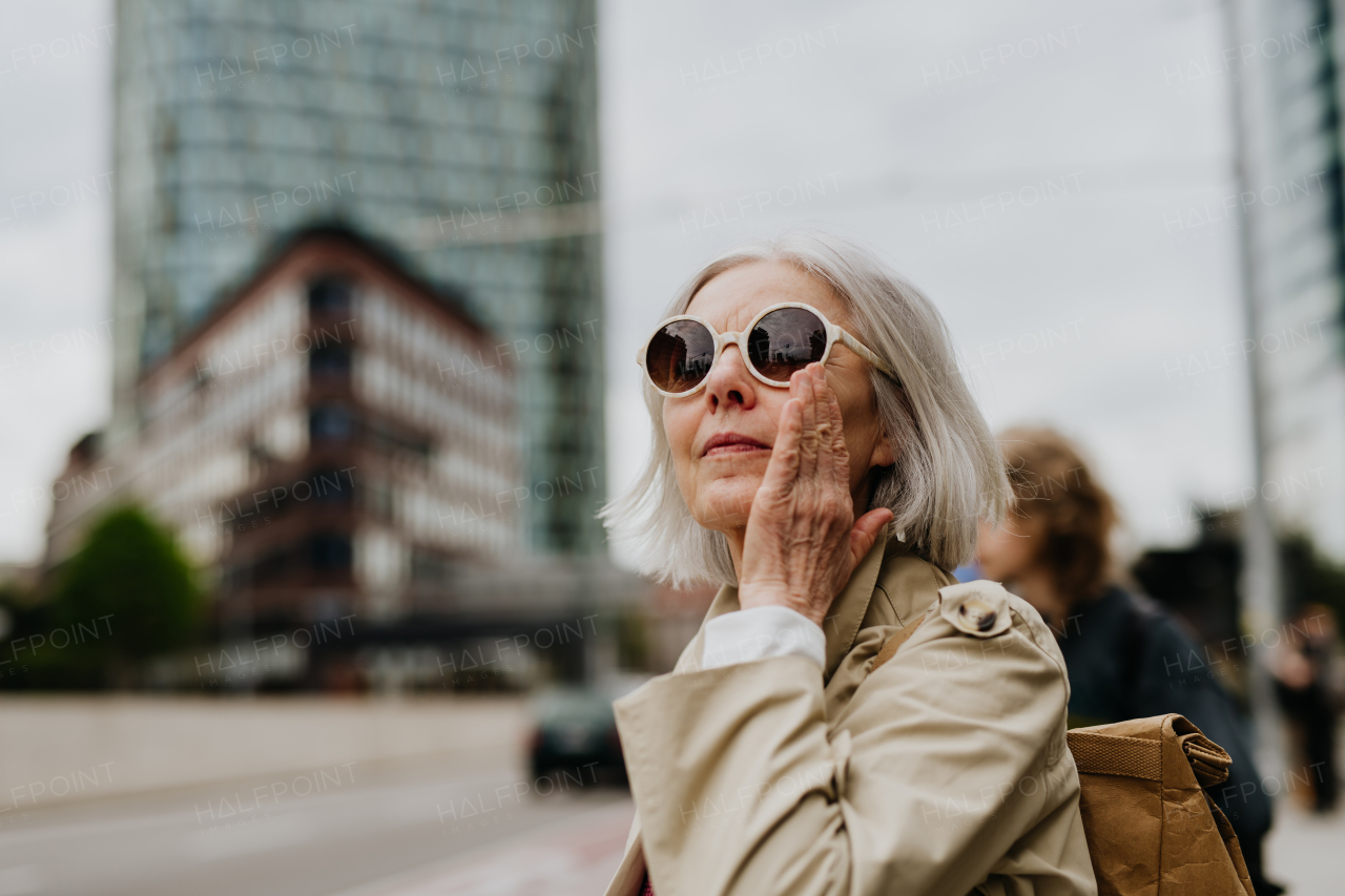 Portrait of stylish mature woman with gray hair on city street. Older woman in sunglasses waiting for public transport, urban commuter.