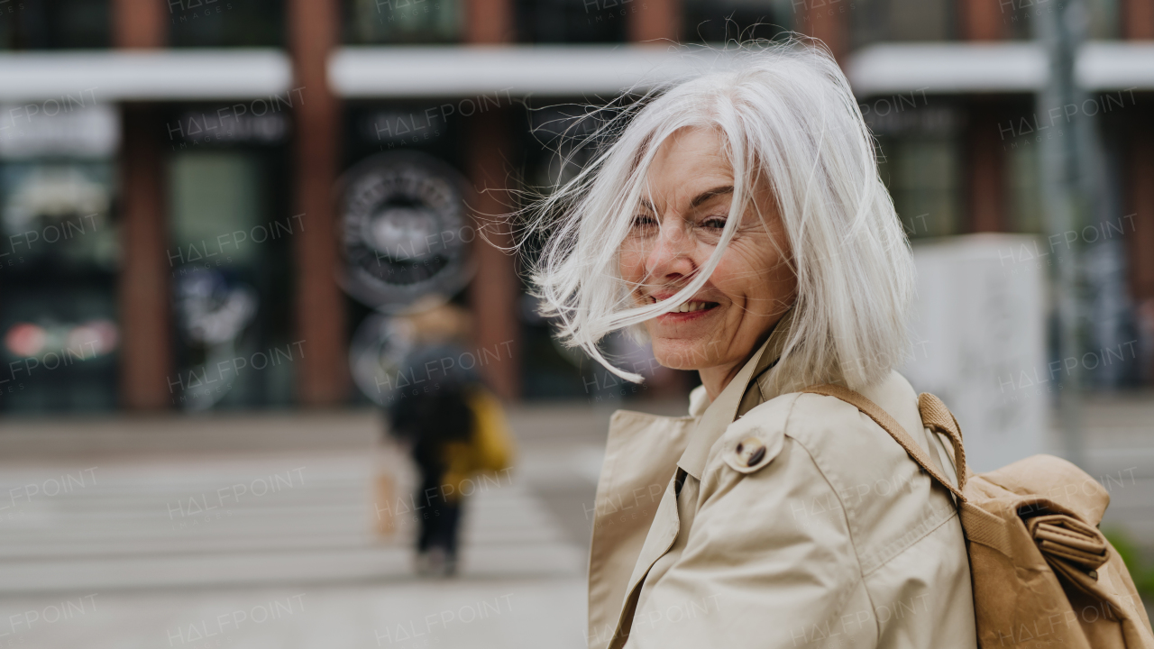 Portrait of stylish mature woman with a gray hair on city street. Stunning woman crossing a road on pedestrian crossing. Banner with copy space.