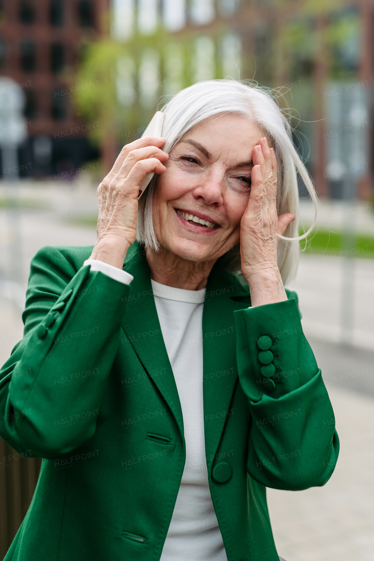 Mature businesswoman phone calling on smartphone, going on business meeting in the city. Beautiful older woman with gray hair standing on city street, smiling.