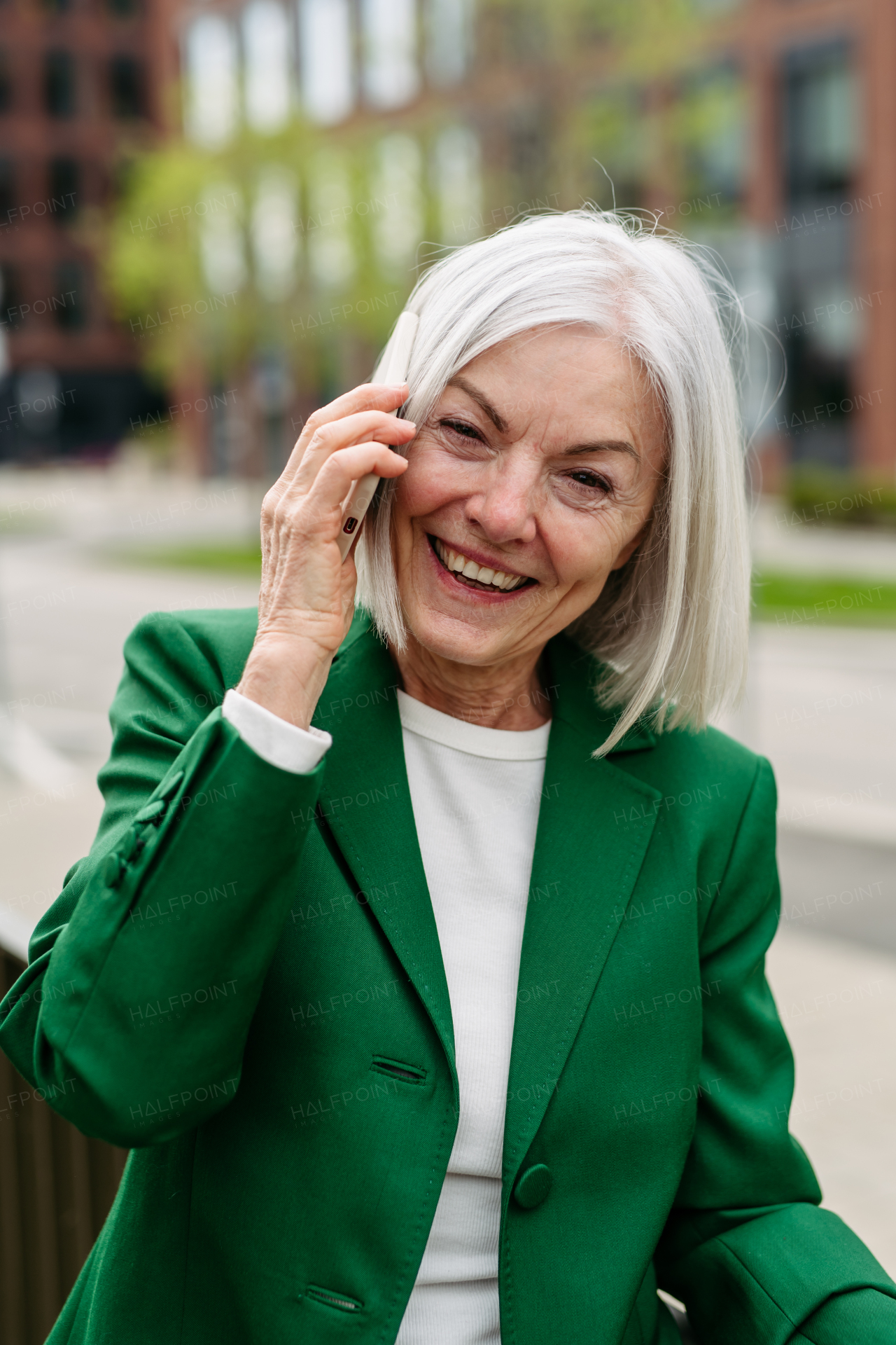 Portrait of mature businesswoman making a phone call on smartphone, going home from work. Beautiful older woman with gray hair on city street.