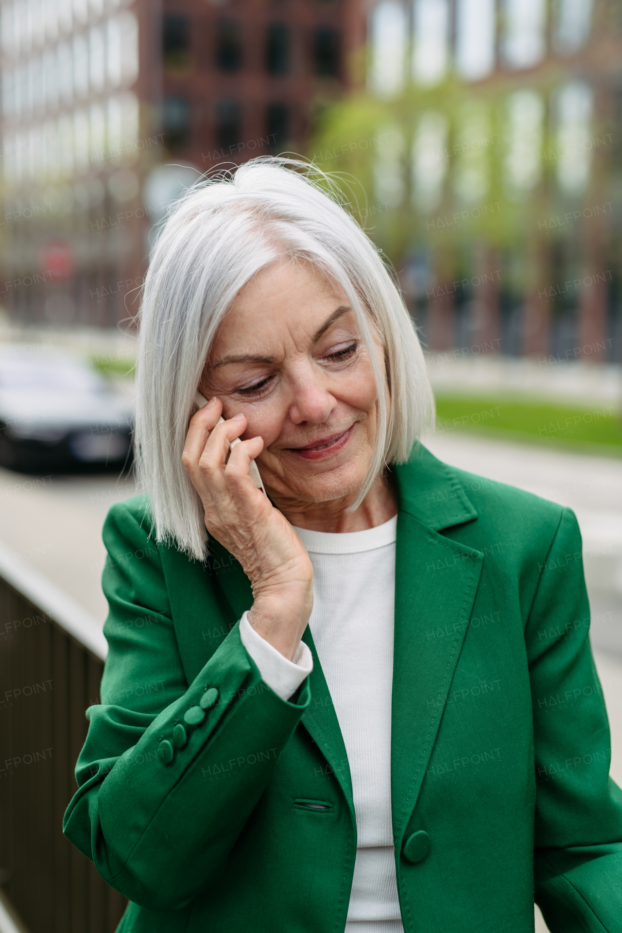 Mature businesswoman phone calling on smartphone, going on business meeting in the city. Beautiful older woman with gray hair standing on city street, smiling.