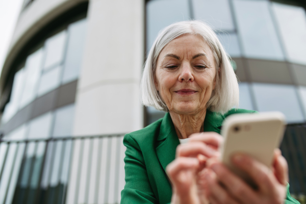 Mature businesswoman holding smartphone, waiting for business partner in the citBeautiful older woman with gray hair standing on city street, smiling.