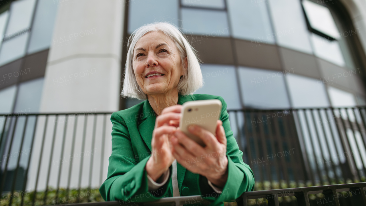 Mature businesswoman holding smartphone, waiting for business partner in the citBeautiful older woman with gray hair standing on city street, smiling.