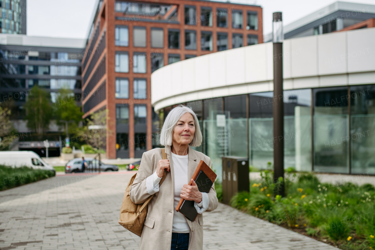 Mature businesswoman going home from work, enjoying beautiful weather and free time. Beautiful older woman with gray hair walking down the city street.