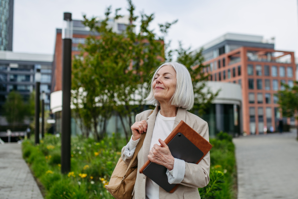 Mature businesswoman going home from work, enjoying beautiful weather and free time. Beautiful older woman with gray hair walking down the city street.