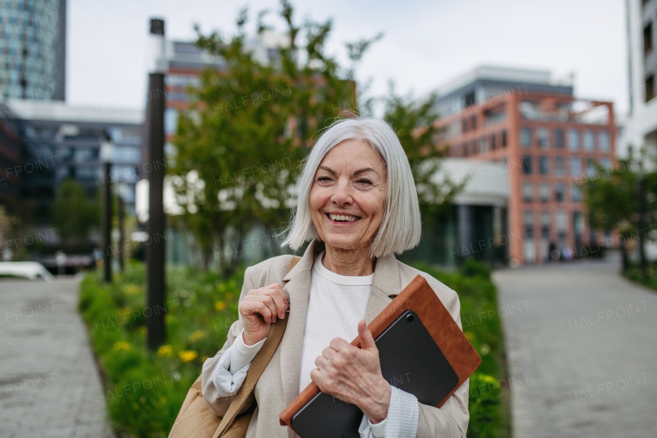 Mature businesswoman scrolling on smartphone, going home from work. Beautiful older woman with gray hair walking down the city street.