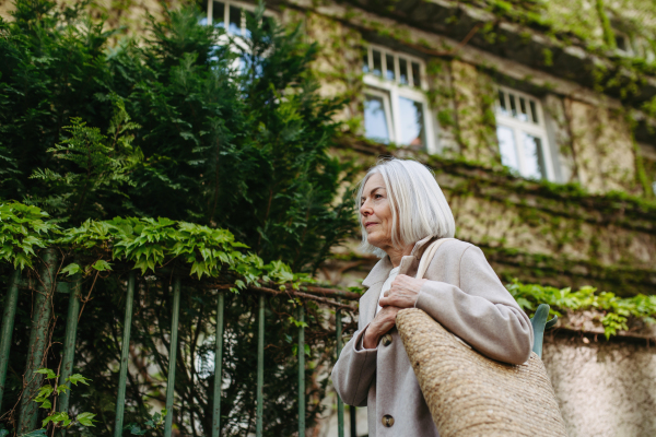 Portrait of stylish mature woman with gray hair on a city street, enjoying beautiful weater during free weekend day.