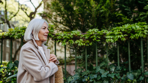 Portrait of stylish mature woman with gray hair on a city street, enjoying beautiful weater during free weekend day.