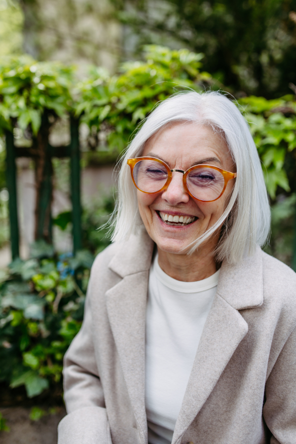 Portrait of stylish mature woman standing on city street.Beautiful older woman with gray hair outdoors, smiling and looking at camera.