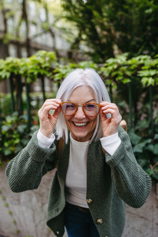 Portrait of stylish mature woman laughing, holding her eyeglasses.Beautiful older woman with gray hair outdoors.