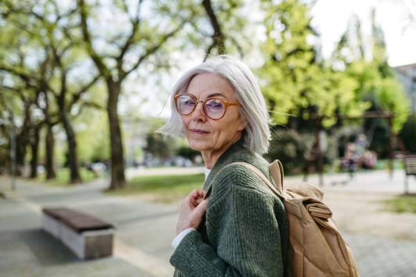 Portrait of stylish mature woman with gray hair on a city street, enjoying beautiful weater during free weekend day.