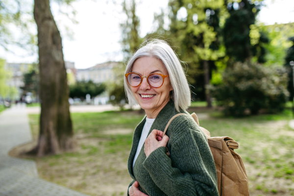 Portrait of stylish mature woman with gray hair on a city street, enjoying beautiful weater during free weekend day.