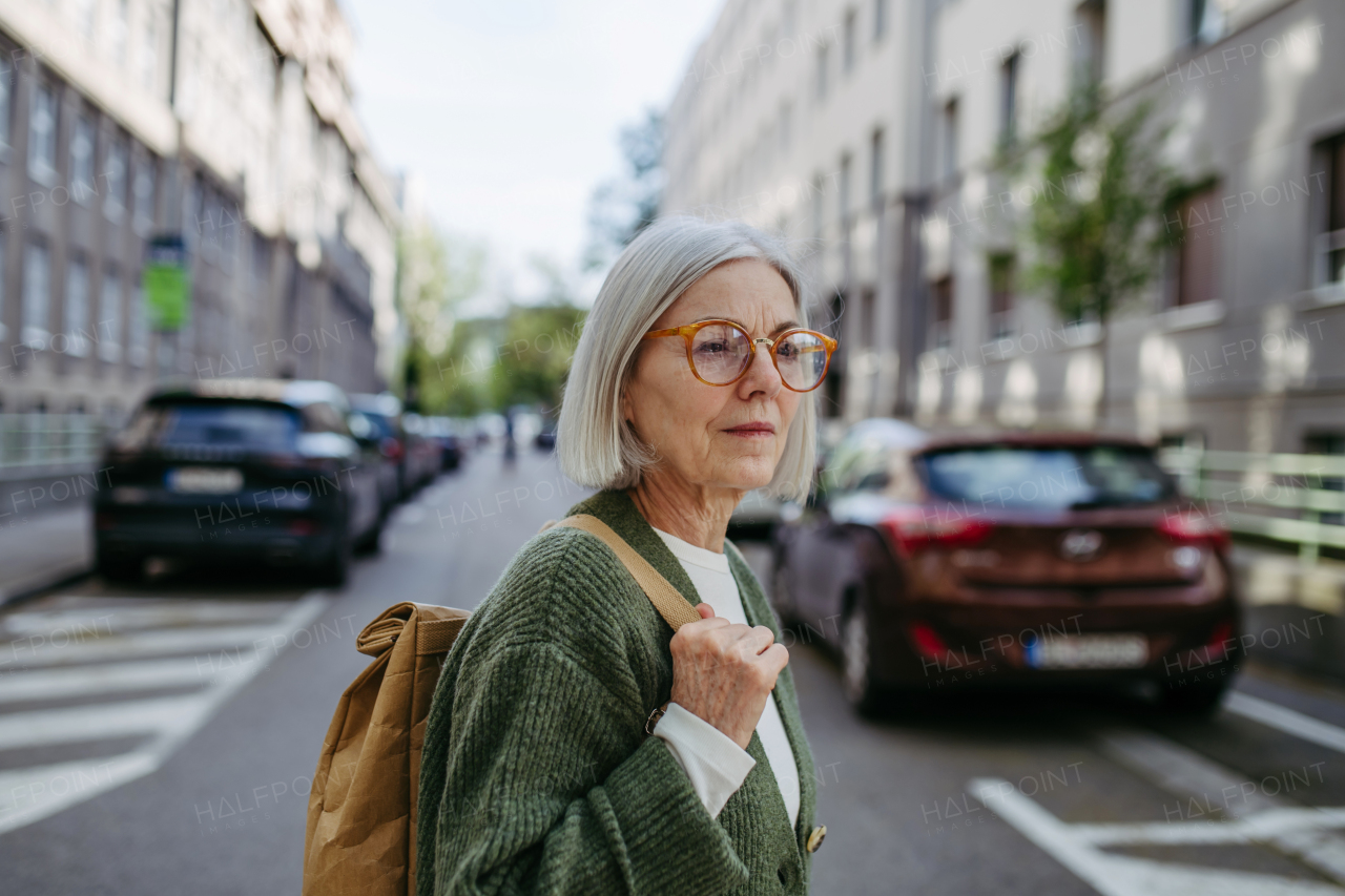 Portrait of stylish mature woman with gray hair on a city street, enjoying beautiful weater during free weekend day.