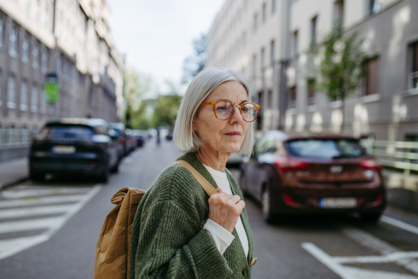 Portrait of stylish mature woman with gray hair on a city street, enjoying beautiful weater during free weekend day.