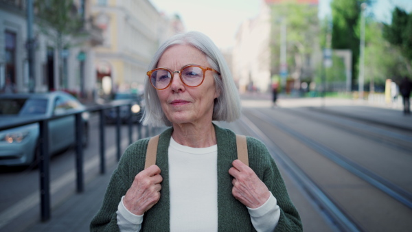 A video of stylish mature woman with gray hair on city street. Older woman with eyeglasses waiting for public transport.