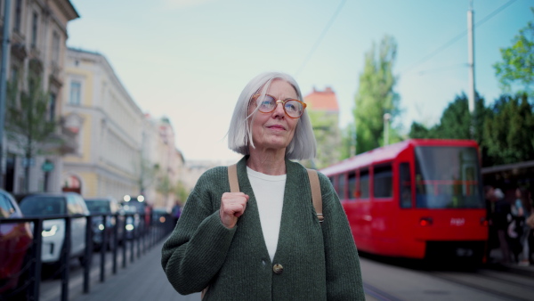 A video of stylish mature woman with gray hair on city street. Older woman with eyeglasses waiting for public transport.