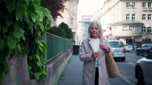 Video of stylish mature woman with gray hair on a city street, enjoying beautiful weater during free weekend day.