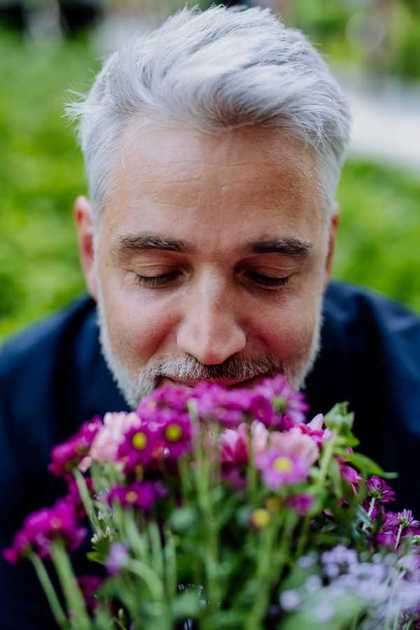 A portrait of happy mature businessman with flower bouquet sitting on bench and waiting for girlfriend.