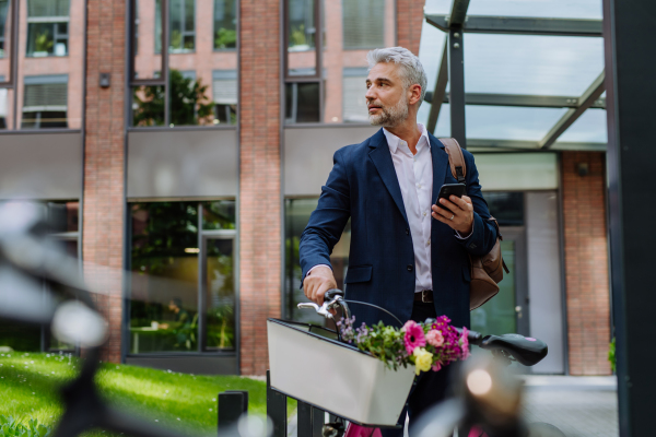 A portrait of happy mature businessman with flower bouquet with bike in street, going to date with his girlfriend.