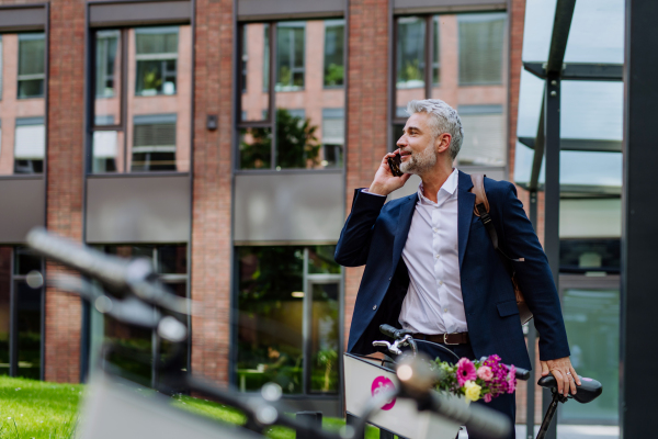 A portrait of happy mature businessman with flower bouquet with bike in street, going to date with his girlfriend.