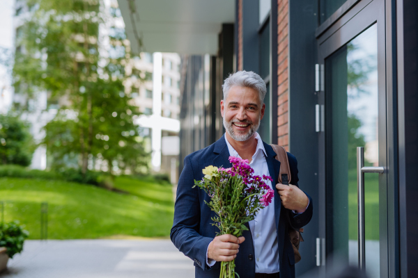 A portrait of happy mature businessman with flower bouquet walking in street to meet his girlfriend.