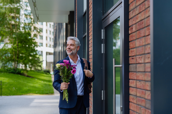 A portrait of happy mature businessman with flower bouquet walking in street to meet his girlfriend.