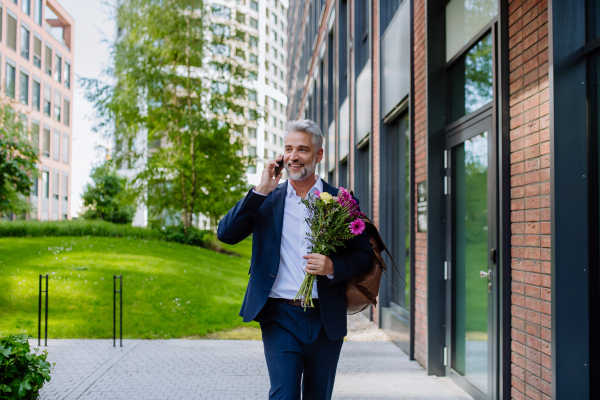 A portrait of happy mature businessman with flower bouquet walking in street to meet his girlfriend.