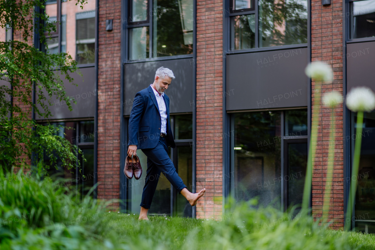 A businessman walking barefoot in park, feeling free, work life balance concept.