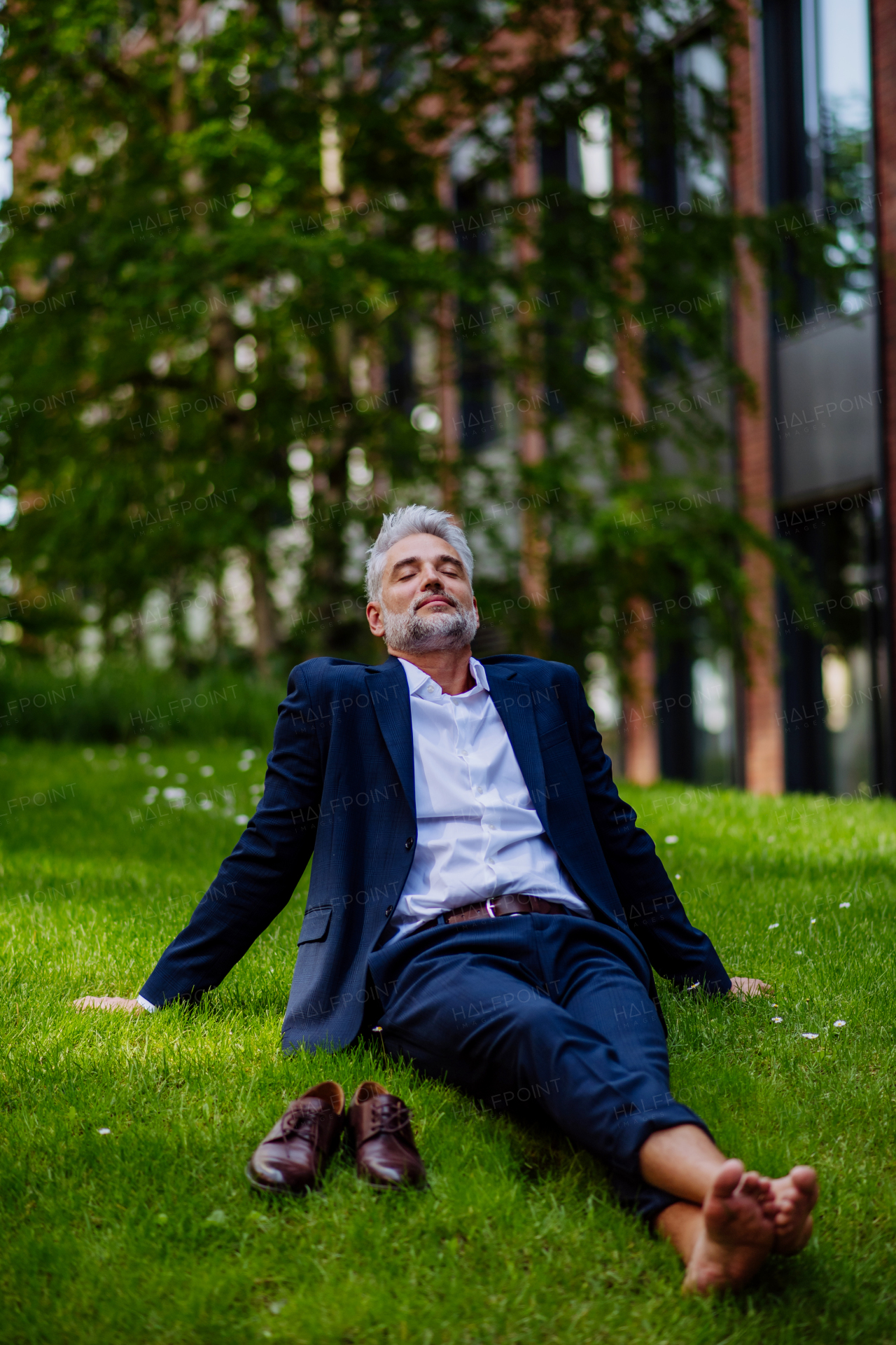 A mature businessman resting and sitting barefoot in park, feeling free, escaping from work, work life balance concept.