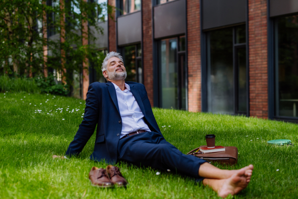 A mature businessman resting and sitting barefoot in park, feeling free, escaping from work, work life balance concept.