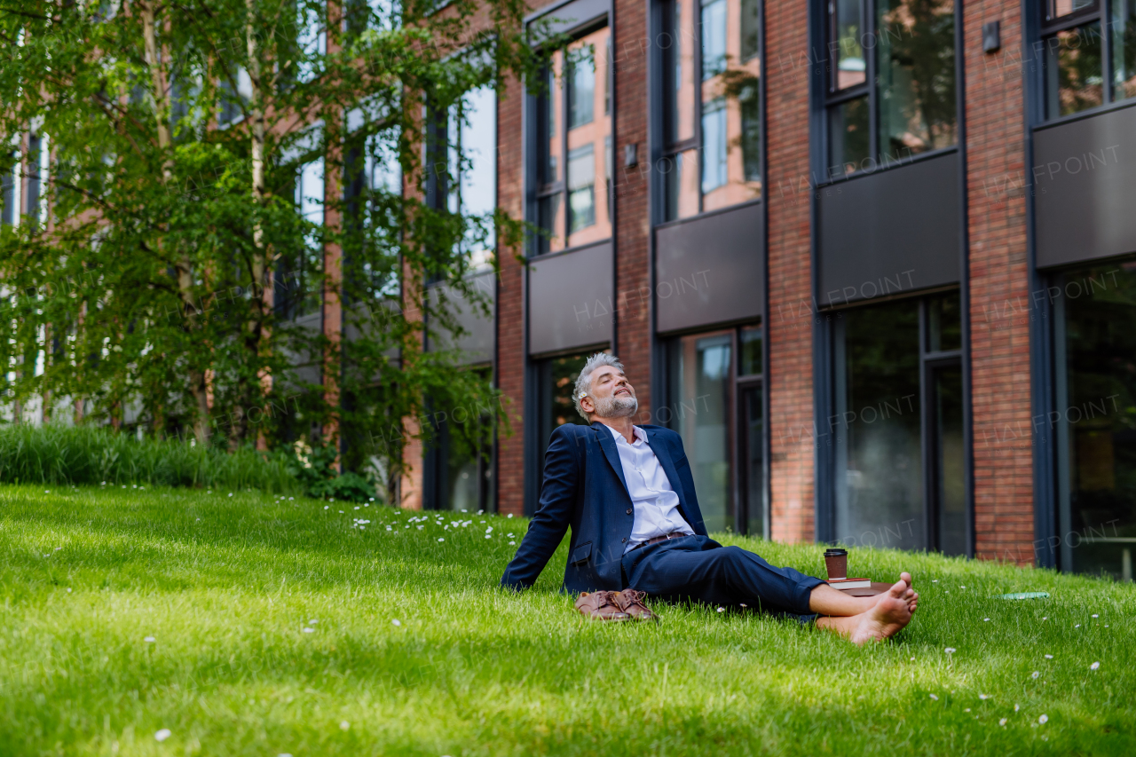 A mature businessman resting and sitting barefoot in park, feeling free, escaping from work, work life balance concept.