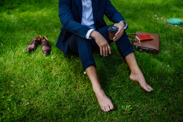 A businessman having coffee, resting and sitting barefoot in park, feeling free, escaping from work, work life balance concept.