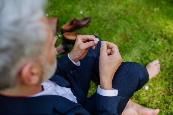 A mature businessman resting and sitting barefoot in park, feeling free, escaping from work, work life balance concept.