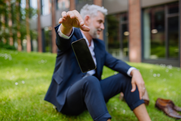 A mature businessman throwing away his smarthpone when sitting barefoot in park, feeling free, escaping from work concept.