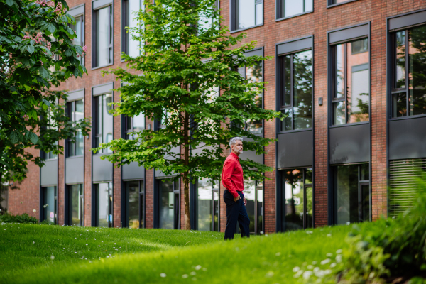 A businessman walking in park near office buliding during break, work life balance concept.