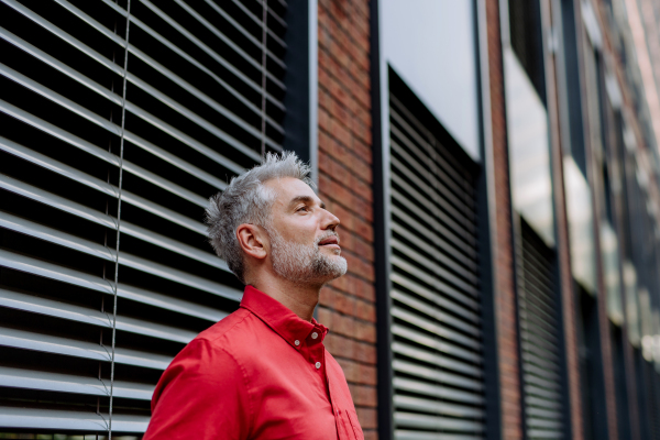 A mature businessman standing on street in front of window with blinders, copy space.