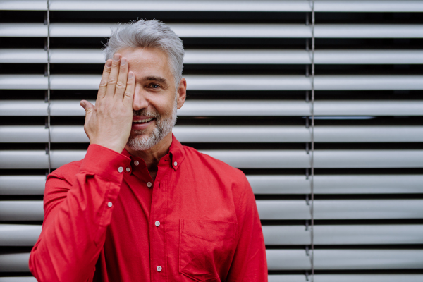 A mature businessman standing on street in front of window with blinders, copy space.