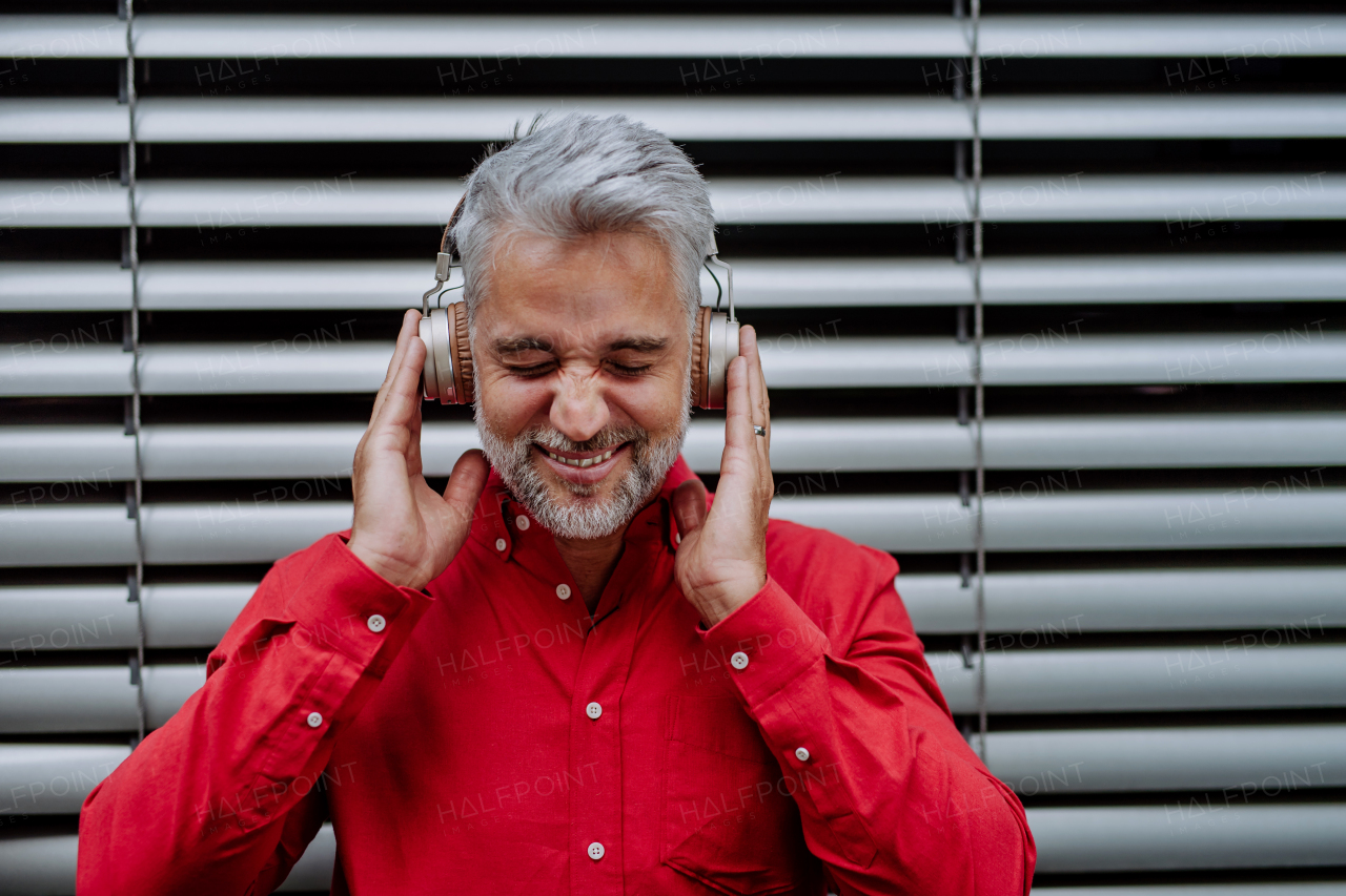 A mature businessman enjoying music in headphones relaxing on balcony during break at work.