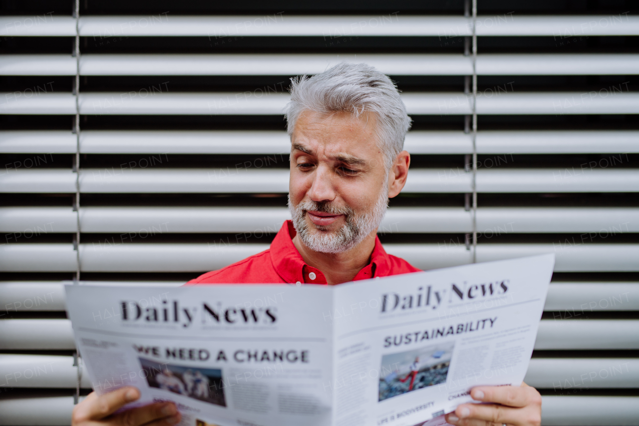 A mature businessman sitting at balocny and reading newspaper.