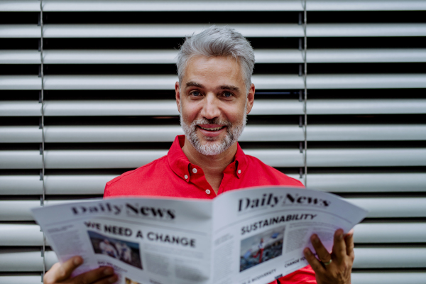 A mature businessman sitting at balocny and reading newspaper.